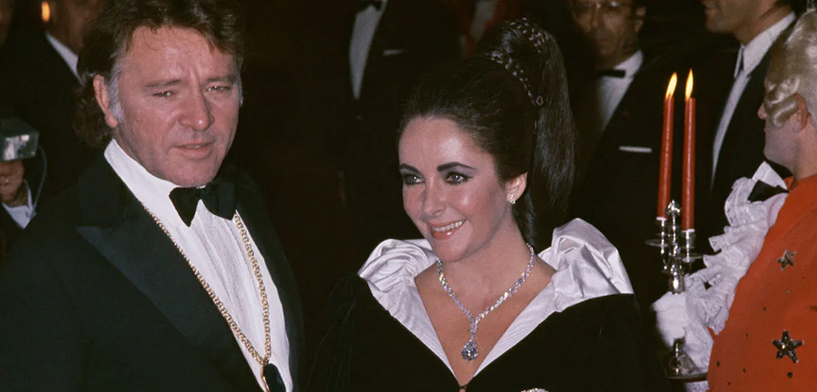 Elizabeth Taylor e Richard Burton durante un evento di gala. Elizabeth indossa il celebre diamante Taylor-Burton, simbolo di lusso e glamour, montato su un collier di platino.