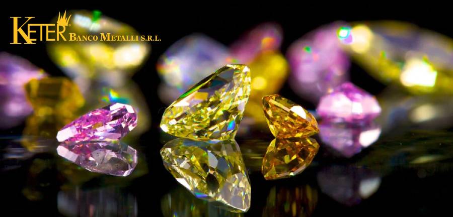 Immagine di diamanti colorati rari e preziosi, con tonalità vivaci di giallo, rosa e arancione, riflessi su una superficie lucida nera. Questi diamanti fancy rappresentano una delle gemme più affascinanti e ricercate nel mondo dell'orologeria e della gioielleria di lusso.