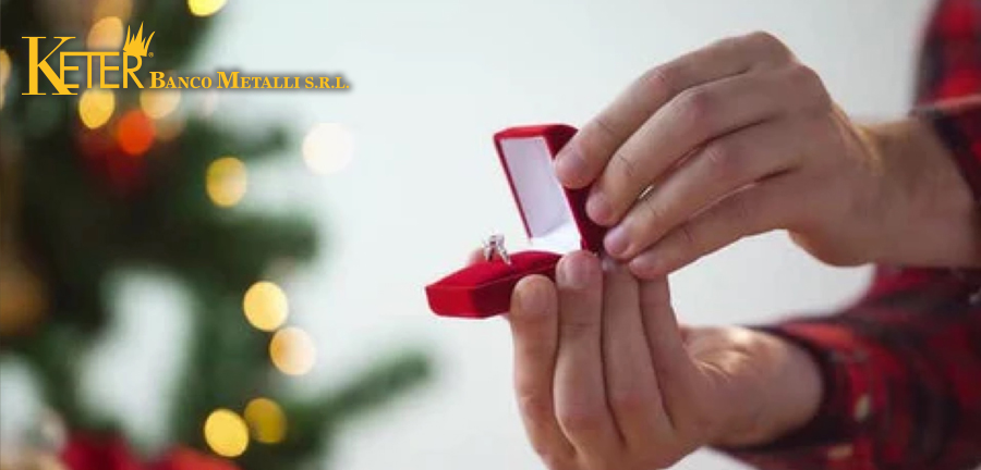 Una persona offre un anello con diamante in una confezione rossa, con un albero di Natale decorato sullo sfondo. L'immagine cattura il momento perfetto per regalare un gioiello durante le festività natalizie.